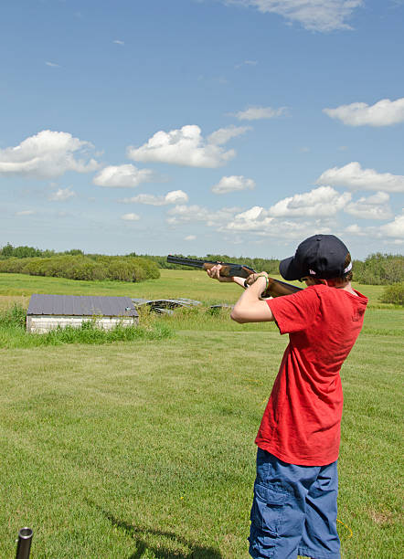 Youth and Summer Trap Shooting A teenage boy shooting Trap. The clay pigeons are mechanically thrown from the machine inclosed in the small shed and shot with a shotgun.  Copy space trap shooting stock pictures, royalty-free photos & images