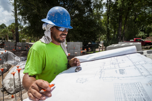 A Hispanic construction supervisor is reviewing a set of plans on a residential construction site in Southwest Florida.