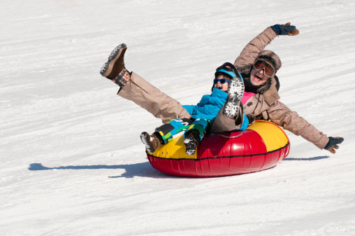 Young woman and little boy sliding down the hill in snow tube