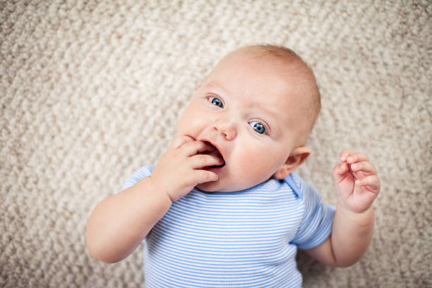 happy baby boy lying on carpet en su hogar - finger in mouth fotografías e imágenes de stock