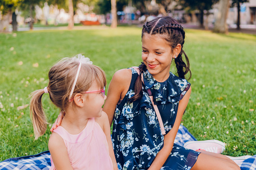 Two little girls enjoy a hug at a picnic in the park.