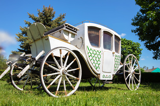 An antique white carriage from the nineteenth century on a green lawn. The prototype of a modern car.