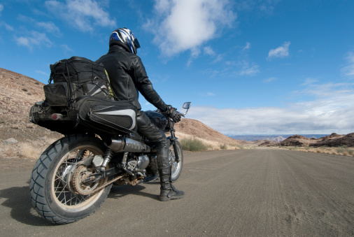 motorcyclist in leathers stops on a dirt road to appreciate the view of the fish river canyon in Namibia. self portrait.