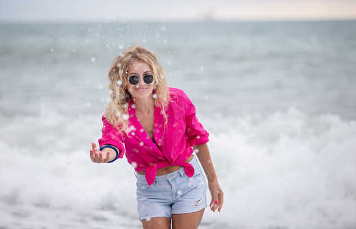 A beautiful woman in sunglasses and a pink shirt splashes sea water.