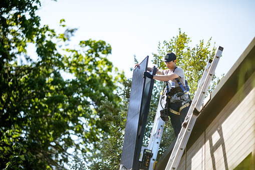 A professional solar panel crew installs panels on the roof of a house in Washington state, USA.  They use a motor powered ladder rig to move the panels from the ground to the roof.  Green environmentally friendly energy.