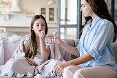 Caring woman bring her sick daughter medication pill and glass of water