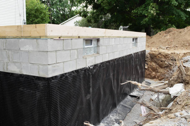 New Basement Foundation A suburban residential construction site new basement foundation with two glass block windows and a durable, heavy-duty plastic basement waterproofing shroud newly installed. excavated material stock pictures, royalty-free photos & images