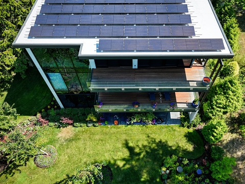 A drone shot of a modern house in the Pacific Northwest with newly installed solar panels installed.  Green environmentally friendly energy.