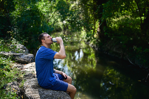 drinking handsome man drinking fresh water on a riverbank.
