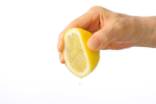 Close-up shot of hand squeezing a lemon isolated on white background.