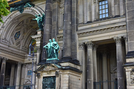 Old darkened facade of the church with columns, arches, sculptures and decor. Protestant Cathedral. Ancient architecture. Germany, Berlin, August 2022.