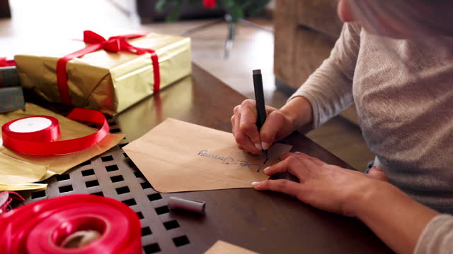 Close up of unrecognizable woman writing a Christmas card and wrapping gifts at home