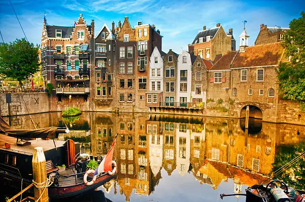 Historic cityscape along a channel in Delfshaven, a district of Rotterdam, the Netherlands. Visible are typical dutch architecture, historic sailing boats, restaurants, colorful reflection in the river, blue and dramatic cloudscape and beautiful sunset atmosphere.
