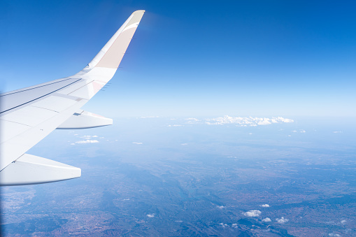View through the window of a commercial airliner, the wing of the aircraft in mid-flight, on a cloudless blue sky day.
