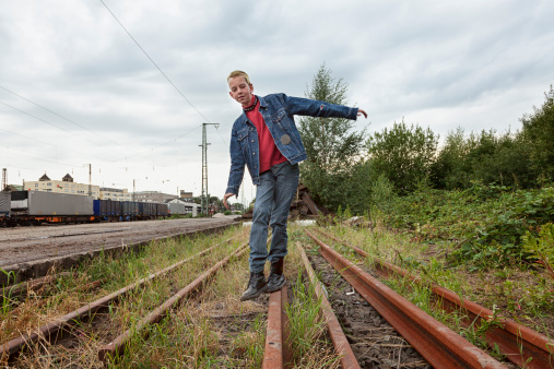 male young teenager with half shaved head, walking over railroad tracks, trying to keep balance
