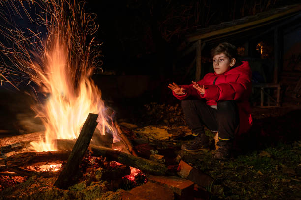 Boy warms his hands near campfire in nature.