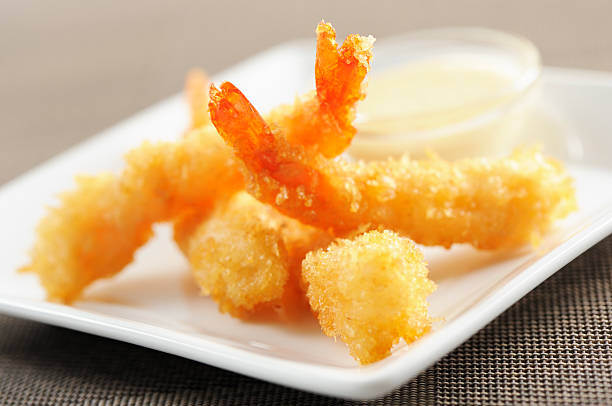 Fried tempura shrimps with sauce out of focus in a white plate.