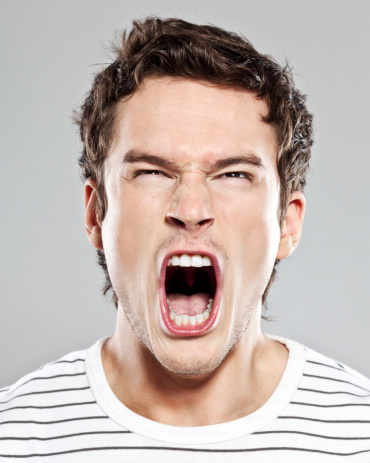 Portrait of frustrated young man screaming at the camera. Studio shot.