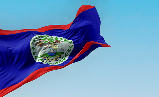 Belize national flag waving in the wind on a clear day. Blue field, red stripes top and bottom, white disk with National Coat of Arms. 3d illustration render. Fluttering fabric