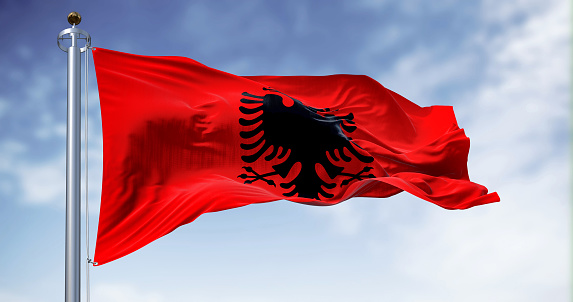 Albanian national flag waving in the wind on a clear day. Red flag with black two-headed eagle. 3d illustration render. Fluttering fabric.