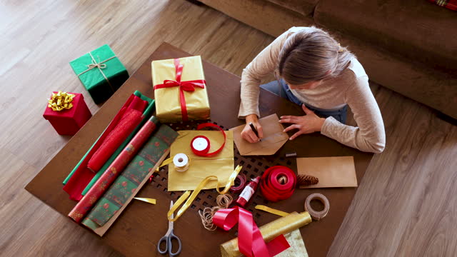 High angle view of woman writing Christmas cards and packing gifts while sitting on the floor at home