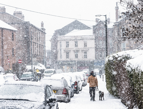 Glasgow, Scotland - Rear view of a man walking with his dog on a street in Partick, during heavy snowfall.