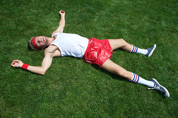 Nerd athlete lies splayed out exhausted in green grass