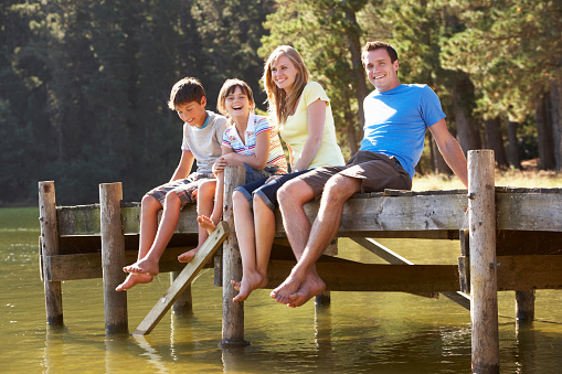 Family Sitting On Wooden Jetty Looking Out Over Lake Laughing