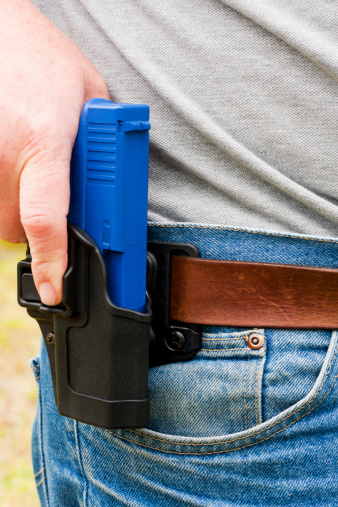 A caucasian man drawing a blue training pistol from a Blackhawk Serpa belt holster, showing proper trigger-finger placement.