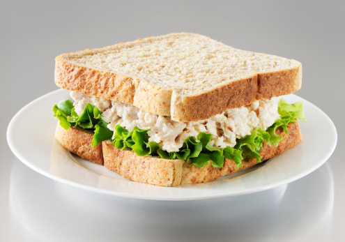 Tuna salad sandwich with leaf lettuce and whole wheat bread on a stainless steel background.