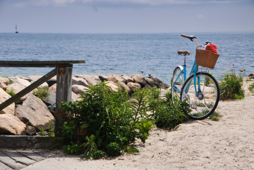 A blue bicycle with a wicker basket with a beach towel stands on a beach in Falmouth, Massachusetts