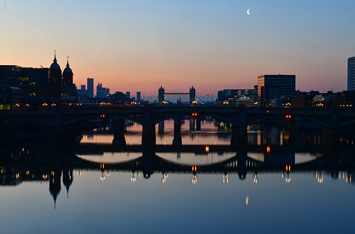 Dawn on the river Thames looking towards London Bridge and distant Tower Bridge under a crescent moon