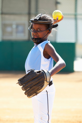 African American girl (9 years) playing softball, wearing face mask (standard safety gear required by many leagues).