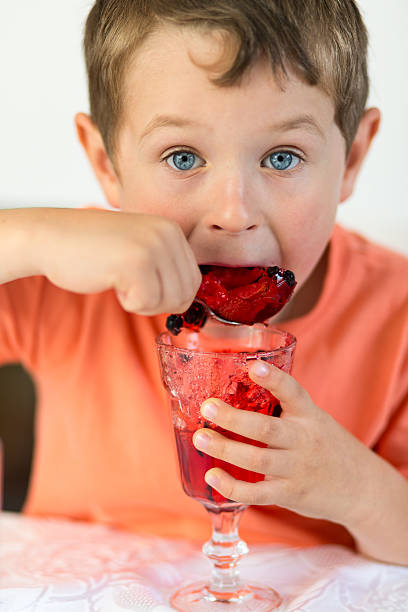 Little boy enjoying a glass of red jelly portrait of small boy eating red jelly little boys blue eyes blond hair one person stock pictures, royalty-free photos & images