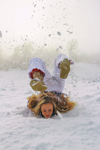Young woman falling over her head into snow. Frozen moment.