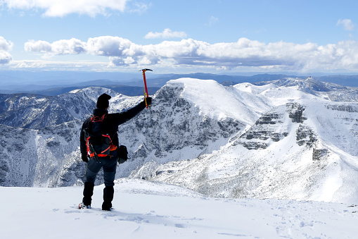 Man with his back on top of a snowy mountain raising an ice axe, Snowy landscape with clouds and blue sky