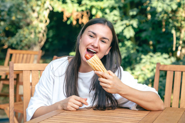 istock A young woman eats a hot dog on a cafe terrace. 1713554618