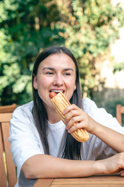 istock A young woman eats a hot dog on a cafe terrace. 1713554625
