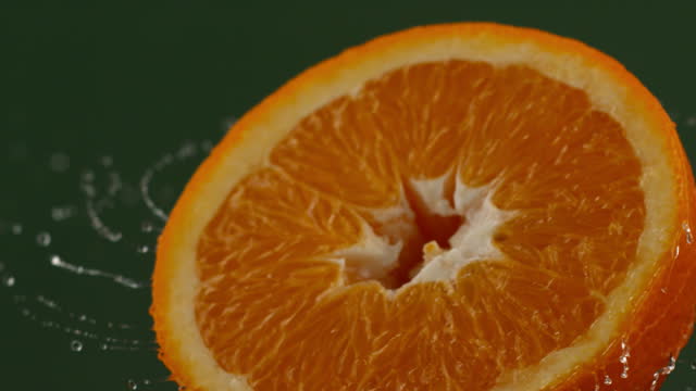 Rotating a wet cut orange in slow motion. Splashing water droplets