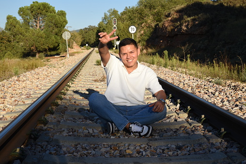 Young young man sitting on the train track on a sunny afternoon, in the mountains