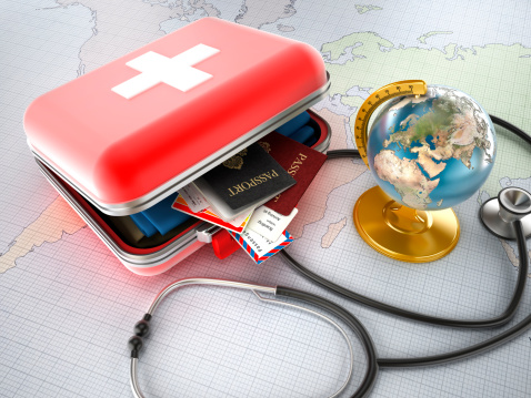 First-aid kit designed as a suitcase with passports, plane tickets and clothes inside, stethoscope and globe standing on world map. Medical tourism concept.