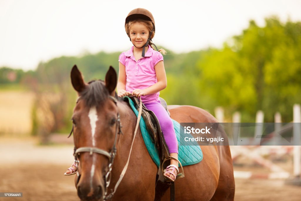 Child Riding Horse Outdoors. Portrait of an cute little girl with riding hat riding horse outdoors. Learning how to ride. Child Stock Photo