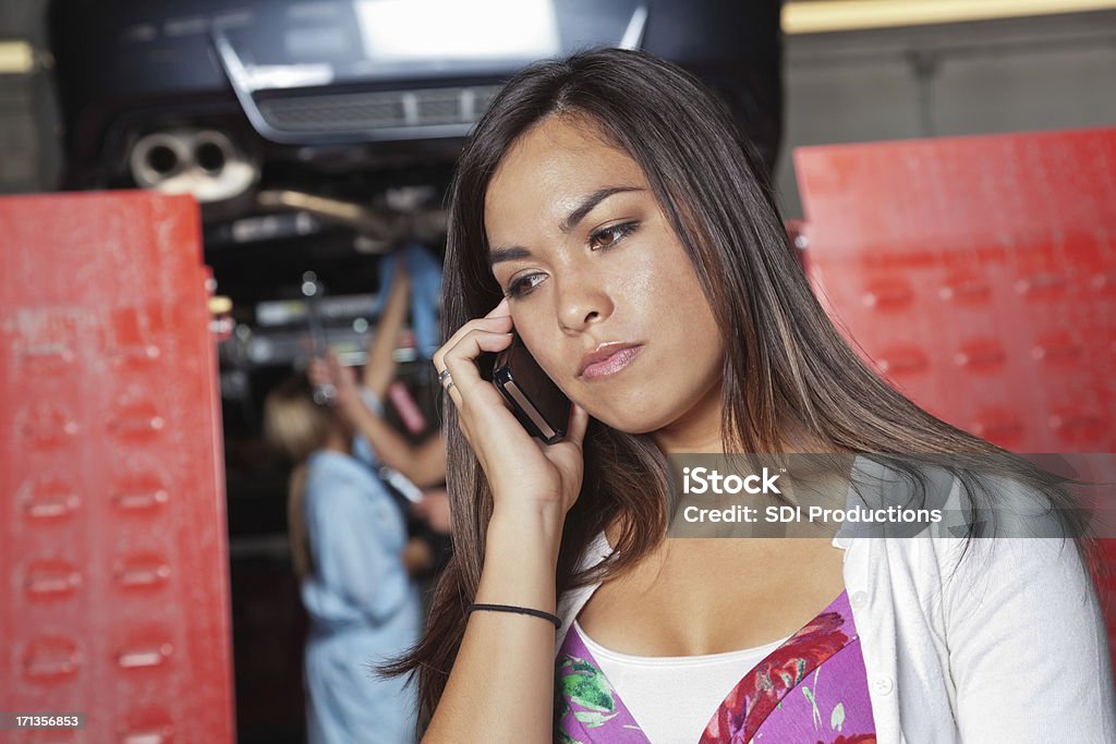 Concerned woman on phone at auto body shop Concerned woman on phone at auto body shop. Adult Stock Photo