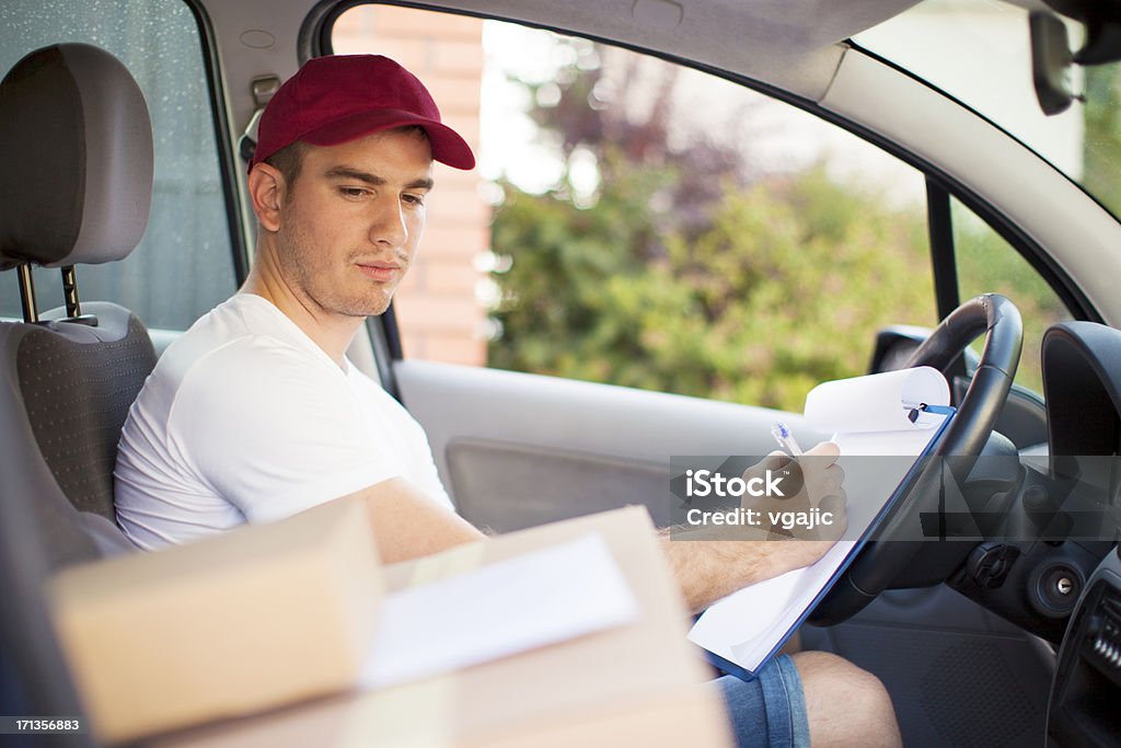 Delivery person inside of a vehicle Delivery man inside of a delivery van, checking addresses for delivery. Selective focus over packages. 20-24 Years Stock Photo