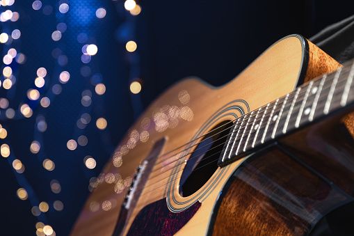 Close-up, acoustic guitar on a dark background with bokeh lights, copy space.