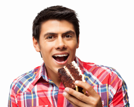 Portrait of young man in casual shirt having a delicious piece of cake. Horizontal shot. Isolated on white.