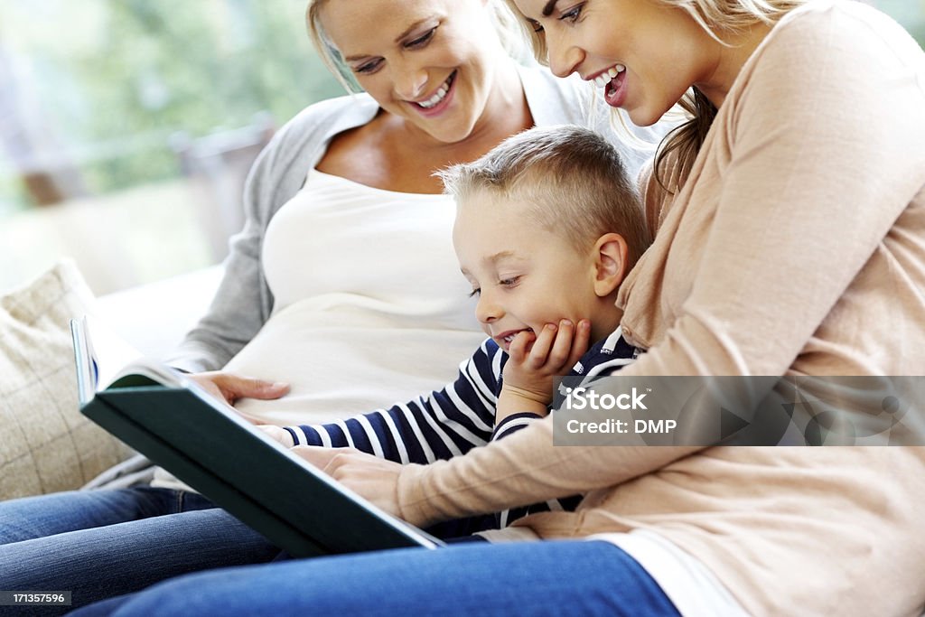 Young family reading story book Young family sitting together on sofa reading a story book at home Abdomen Stock Photo