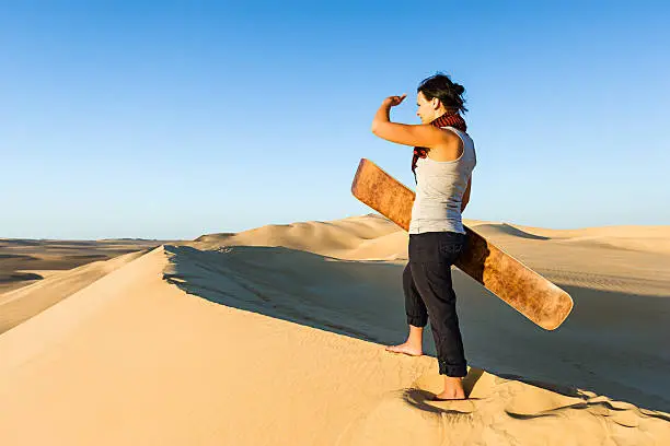 Young female sandboarding in The Sahara Desert. The Sahara Desert is the world's largest hot desert with the biggest sand dunes.