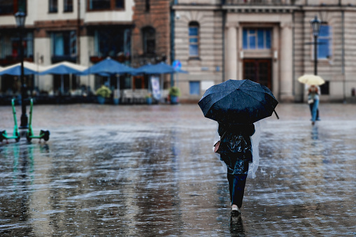 A woman walks down the street with an umbrella in bad rainy weather. Cityscape in rainy weather. City scenes in the rain.