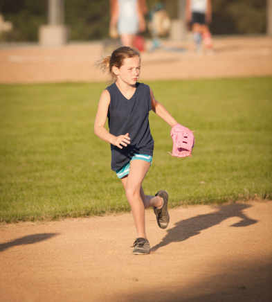 Subject: A young girl with softball mitt catching ball in infield in softball tournament game.